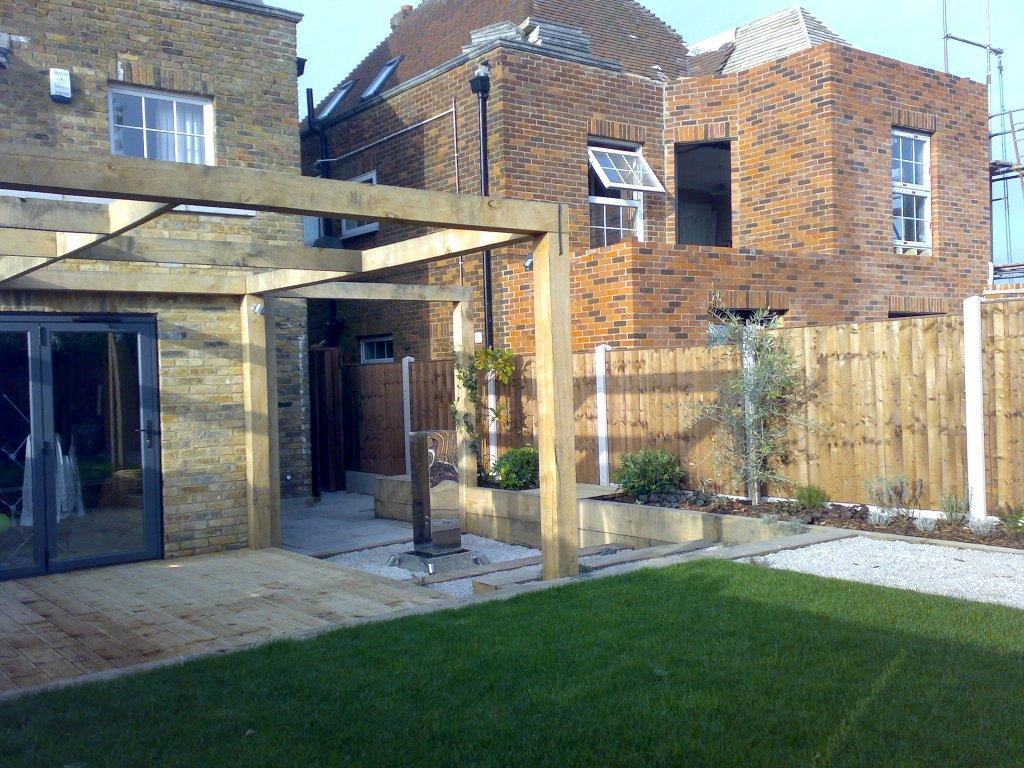 View of garden looking back to the house across the winding shady walk path with shrubs and softwood post crossroad feature in midgorund